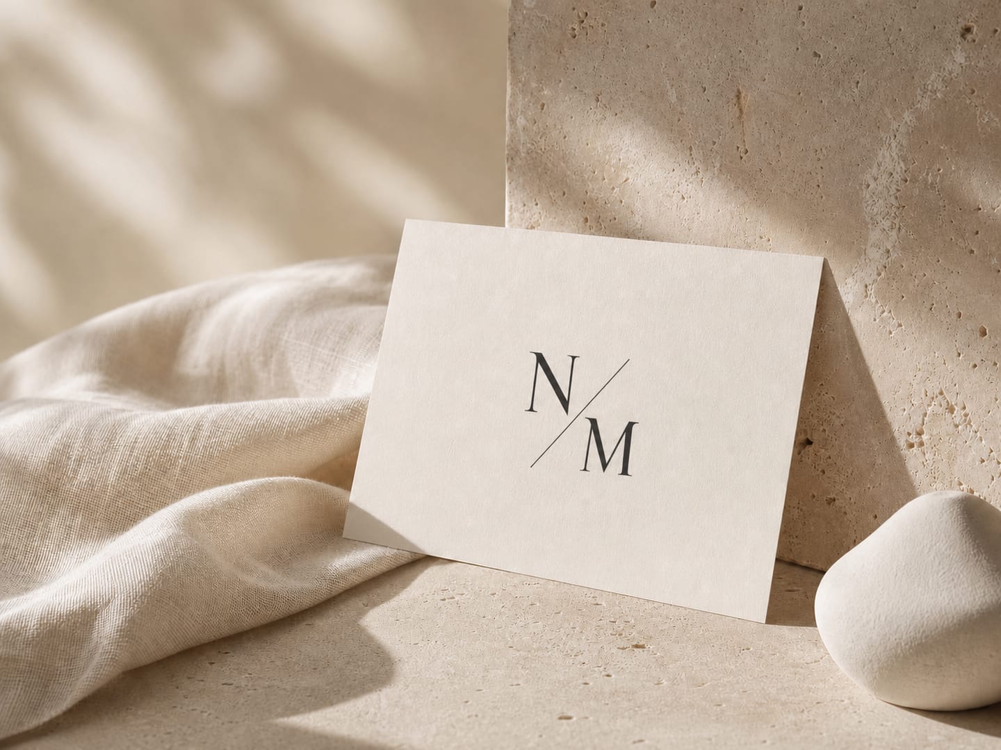 Kremowa karta z monogramem NMANICURE, kamień i miękka tkanina w ciepłym świetle